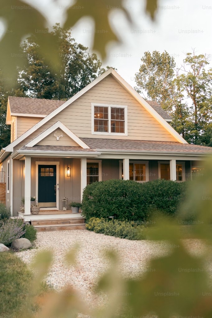 A well-kept craftsman cottage at dusk with a navy door and warm porch lights